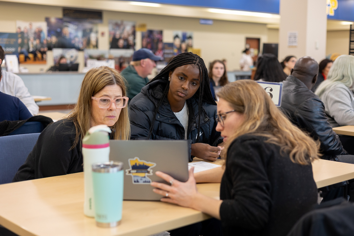 A counselor sitting at a table with a student, pointing at a laptop.