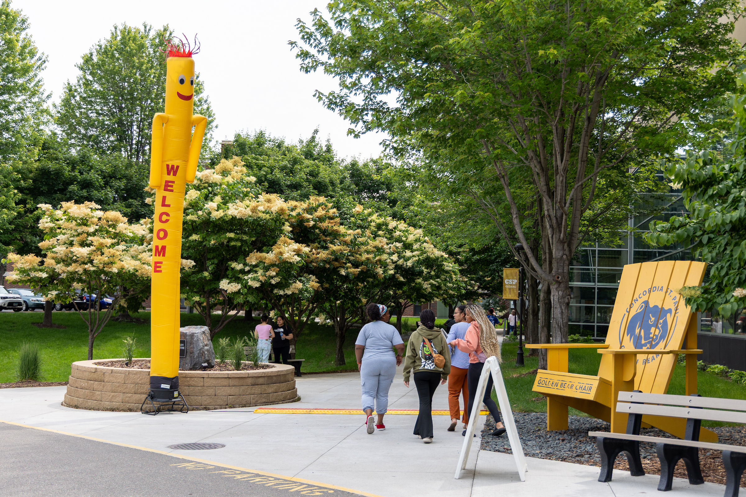 Students on the CSP campus walking toward the entrance to the Library Technology Center, passing a large, golden adirondack chair.