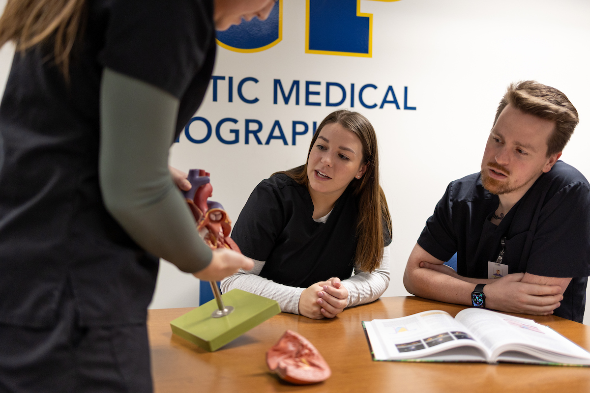 Three DMS students sitting together at a table, looking at a model of a heart together.