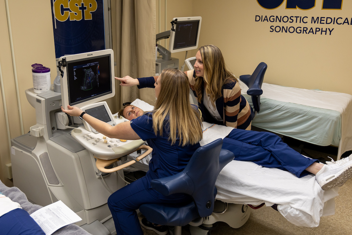 Three DMS students looking at and working with a sonography machine.