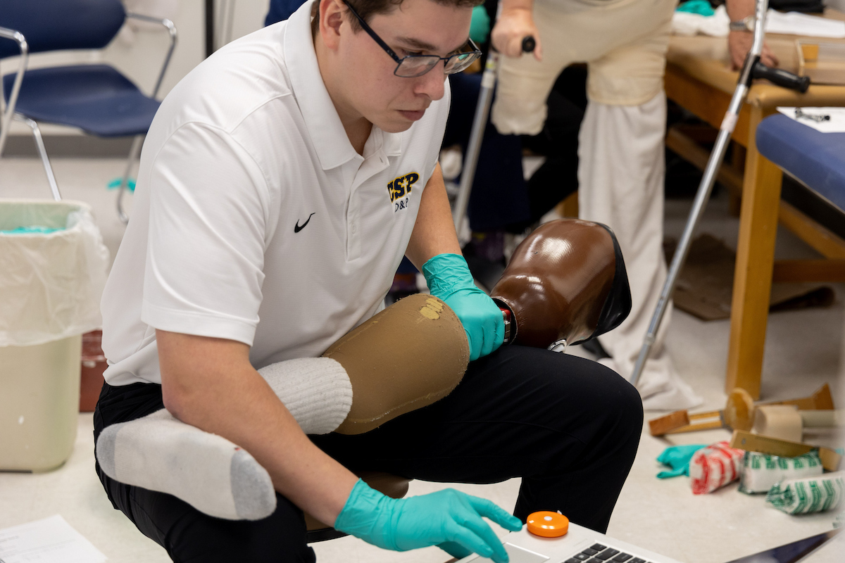 An MSOP student kneeling with a prosthetic leg in their lap.